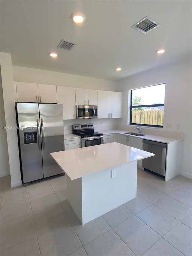 kitchen with a kitchen island, white cabinetry, appliances with stainless steel finishes, light tile patterned floors, and sink