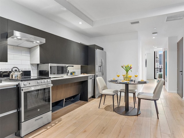 kitchen with dark cabinets, under cabinet range hood, stainless steel appliances, light countertops, and modern cabinets