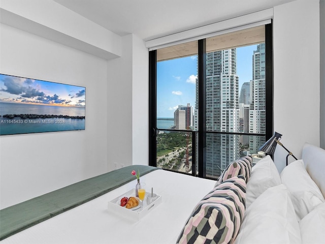 bedroom featuring a water view, multiple windows, a wall of windows, and a city view