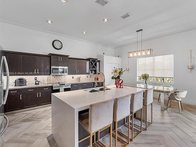 kitchen with appliances with stainless steel finishes, dark brown cabinets, sink, a kitchen island with sink, and light parquet floors