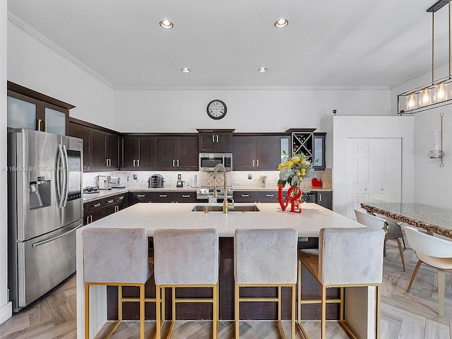 kitchen with light parquet flooring, a kitchen island with sink, appliances with stainless steel finishes, and dark brown cabinets