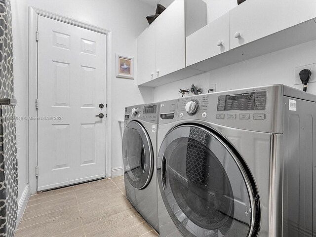 laundry room featuring washer and clothes dryer, light tile patterned floors, and cabinets