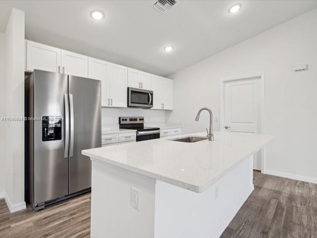 kitchen featuring appliances with stainless steel finishes, vaulted ceiling, a center island with sink, and white cabinets