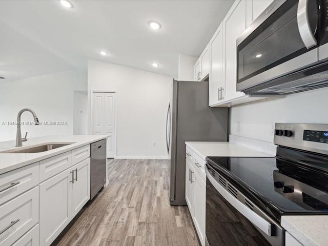 kitchen with white cabinets, light hardwood / wood-style flooring, vaulted ceiling, appliances with stainless steel finishes, and sink