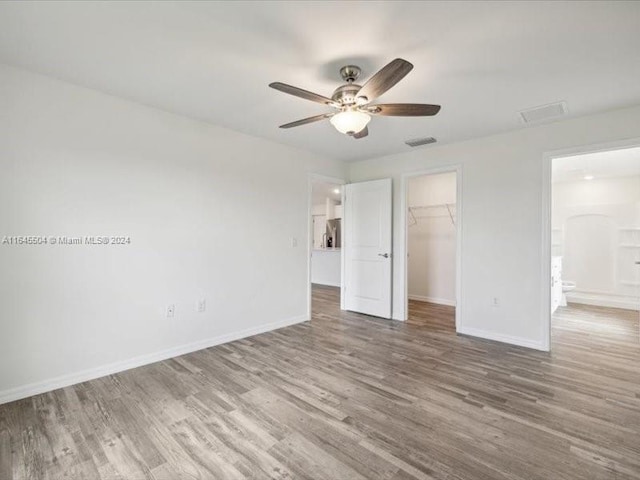 unfurnished bedroom with a closet, ceiling fan, hardwood / wood-style flooring, and a spacious closet