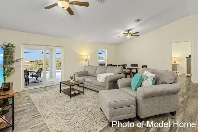 living room with light wood-type flooring, vaulted ceiling, a healthy amount of sunlight, and ceiling fan