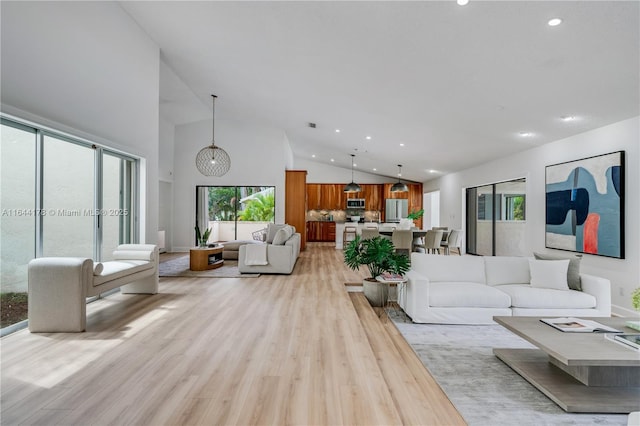 living area with high vaulted ceiling, light wood finished floors, and recessed lighting