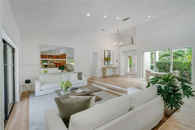 living room featuring visible vents, a high ceiling, light wood-type flooring, a notable chandelier, and recessed lighting