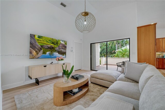 living area with a towering ceiling, light wood finished floors, baseboards, and visible vents