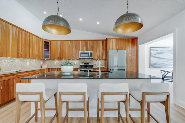 kitchen featuring brown cabinets, stainless steel appliances, lofted ceiling, a sink, and an island with sink