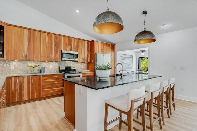 kitchen with stainless steel appliances, brown cabinetry, a sink, and decorative backsplash