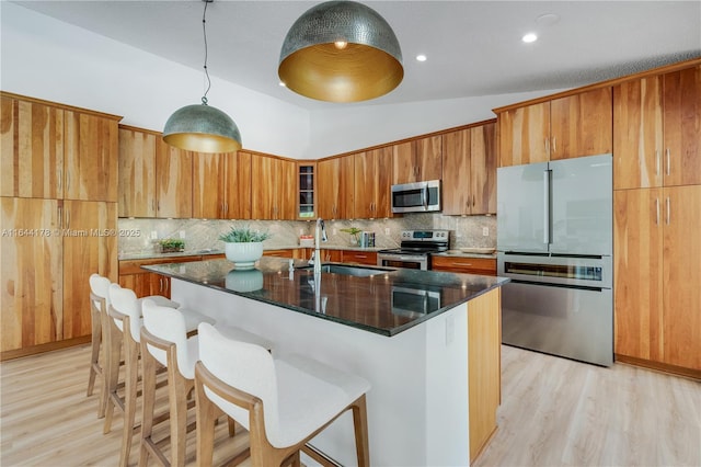 kitchen featuring light wood-style flooring, a breakfast bar, a sink, appliances with stainless steel finishes, and brown cabinetry