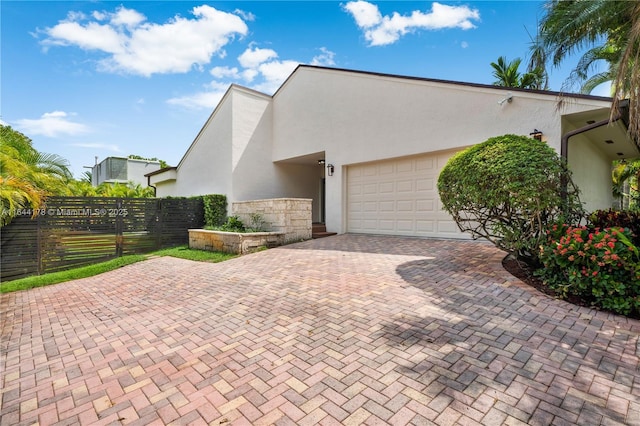 view of front of property featuring decorative driveway, fence, an attached garage, and stucco siding