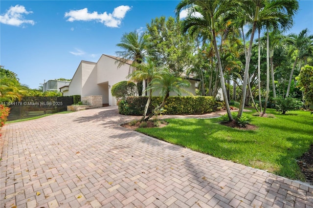 view of front facade featuring decorative driveway, stucco siding, fence, stone siding, and a front lawn