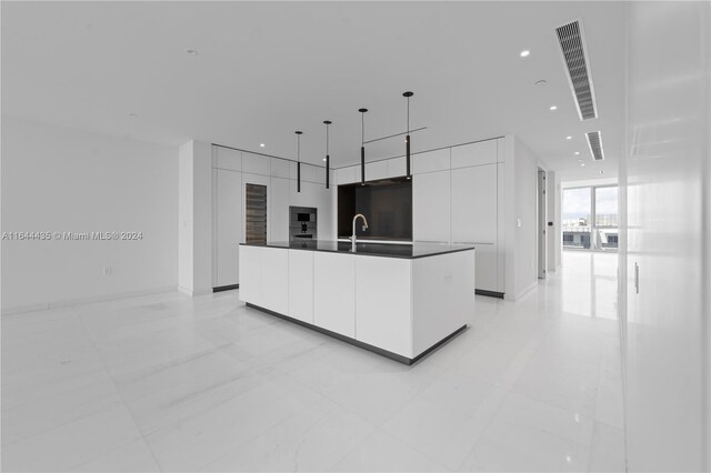 kitchen featuring decorative light fixtures, sink, an island with sink, black microwave, and white cabinets