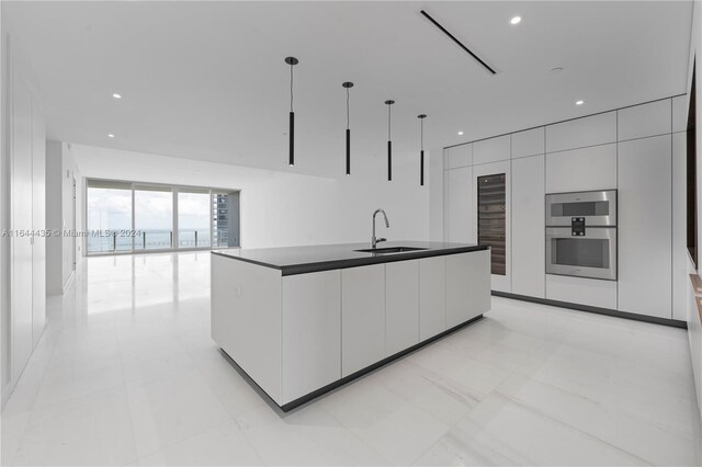 kitchen with pendant lighting, an island with sink, sink, stainless steel double oven, and white cabinets