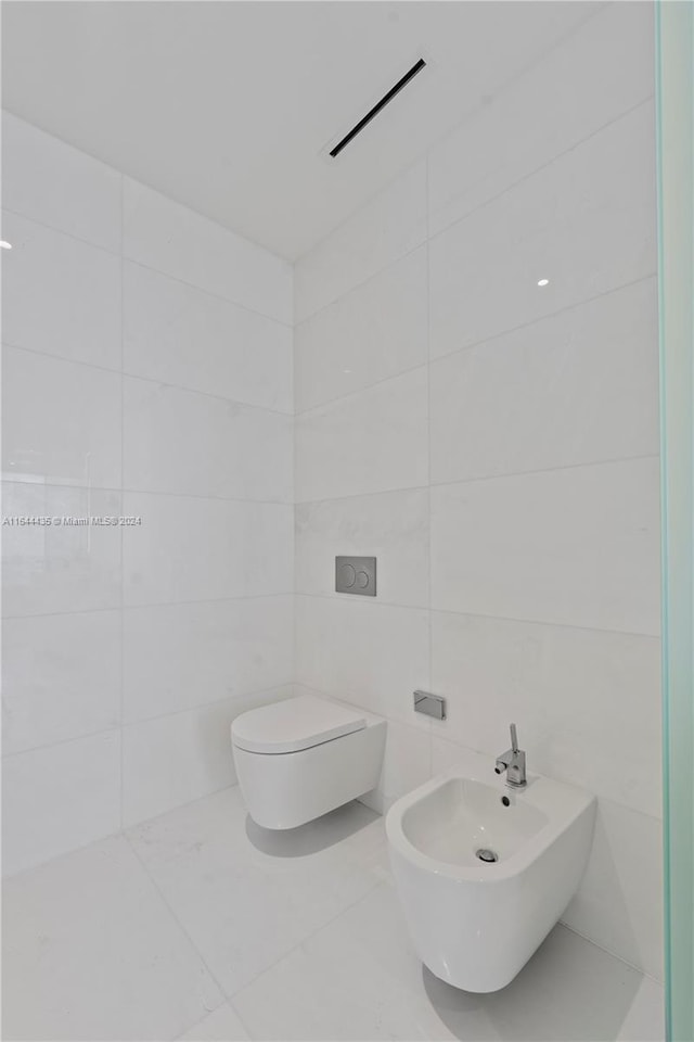 bathroom with a bidet, toilet, and tile walls