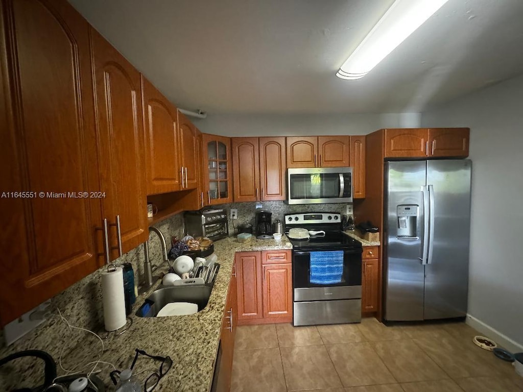 kitchen featuring backsplash, sink, appliances with stainless steel finishes, light stone counters, and light tile patterned floors