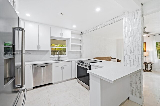 kitchen featuring sink, white cabinetry, appliances with stainless steel finishes, light tile patterned floors, and kitchen peninsula