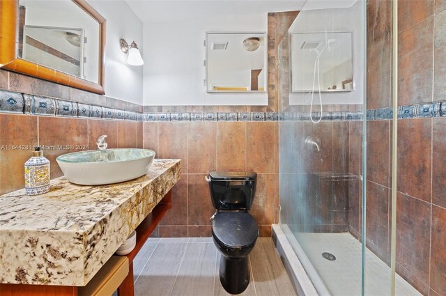 bathroom featuring a shower with shower door, tasteful backsplash, vanity, tile walls, and toilet