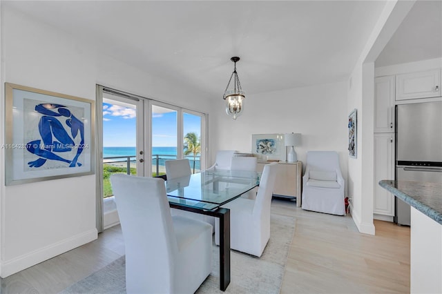 dining area with light wood-type flooring, french doors, a chandelier, and a water view