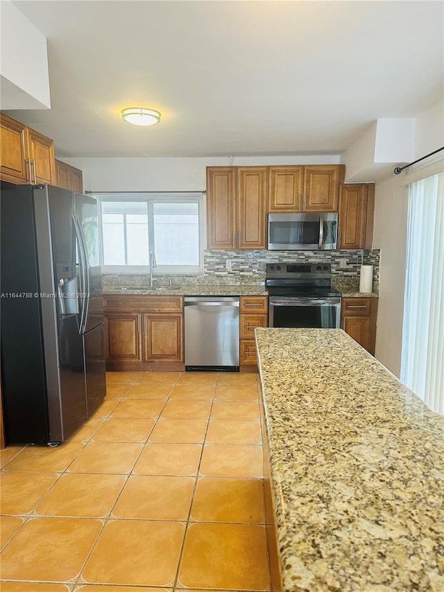 kitchen with light stone countertops, light tile patterned floors, appliances with stainless steel finishes, sink, and decorative backsplash