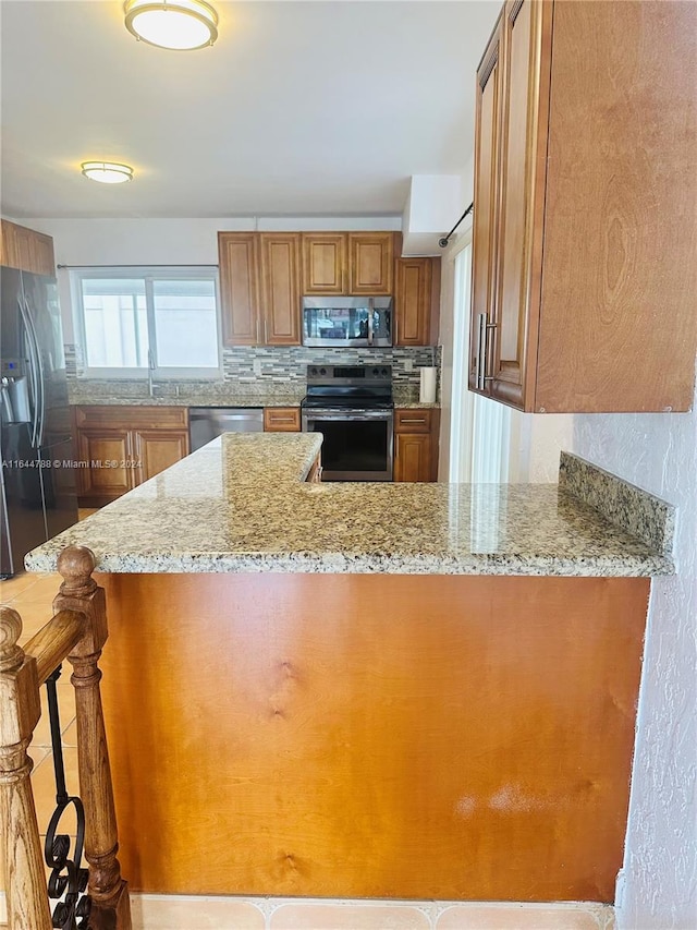 kitchen with backsplash, light stone counters, stainless steel appliances, sink, and a breakfast bar area