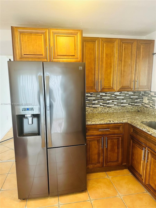 kitchen featuring stainless steel fridge, light stone counters, backsplash, and light tile patterned flooring