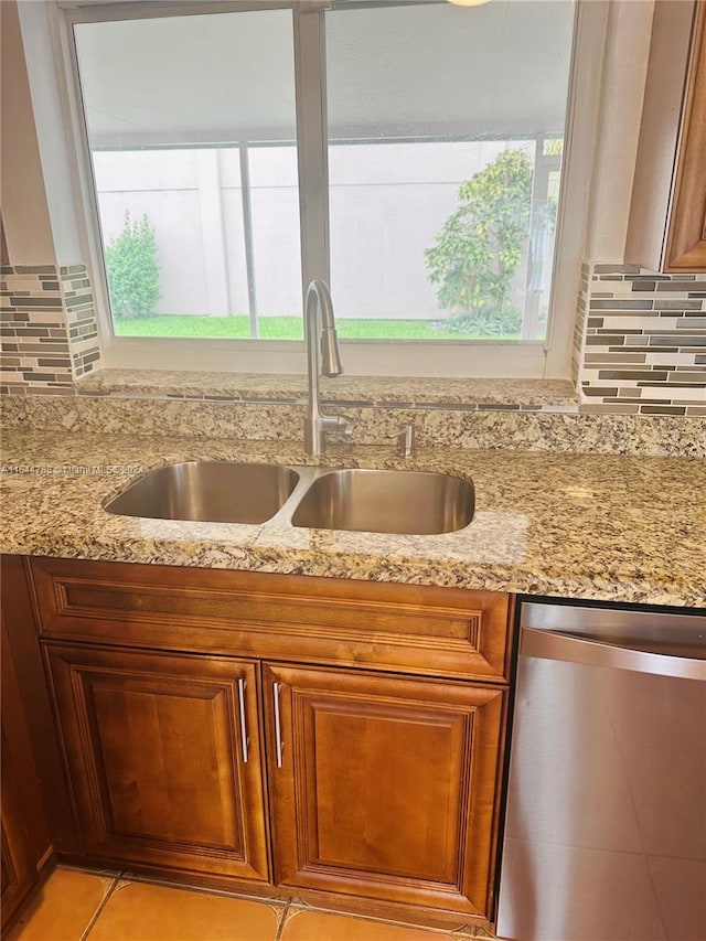 kitchen featuring backsplash, light tile patterned floors, dishwasher, light stone countertops, and sink