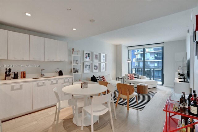 kitchen with sink, light hardwood / wood-style floors, a wall of windows, and white cabinetry