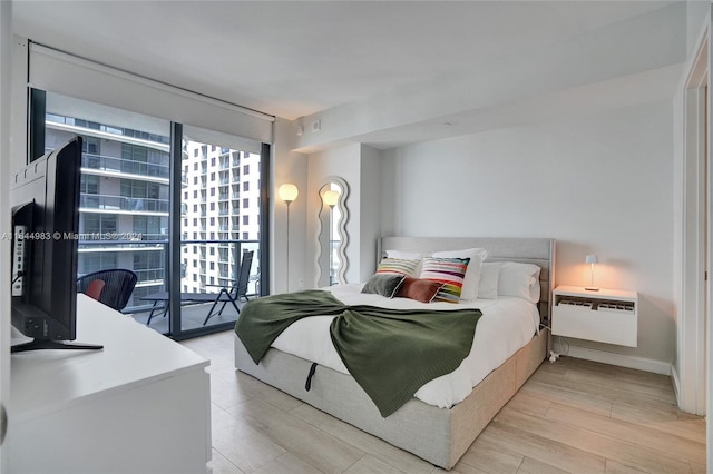 bedroom with baseboards, light wood-style floors, access to outside, expansive windows, and a wall mounted air conditioner