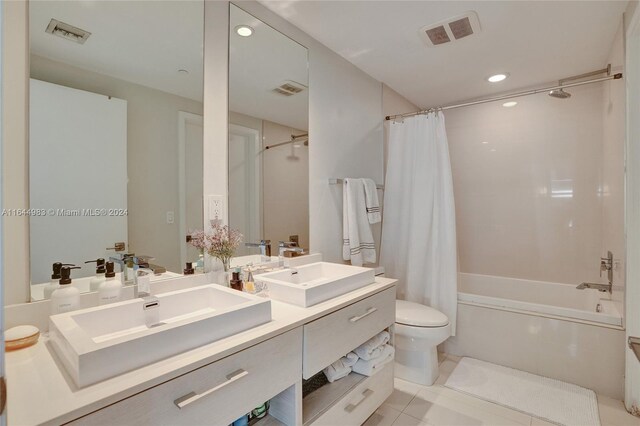 full bathroom featuring toilet, double sink vanity, shower / bath combo with shower curtain, and tile patterned floors