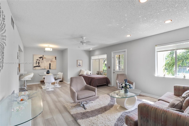 living room with a textured ceiling, light hardwood / wood-style flooring, and ceiling fan