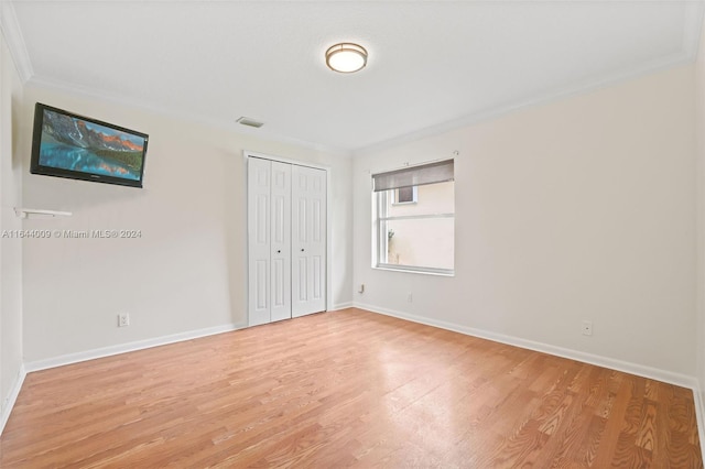 unfurnished bedroom with light wood-type flooring, ornamental molding, and a closet