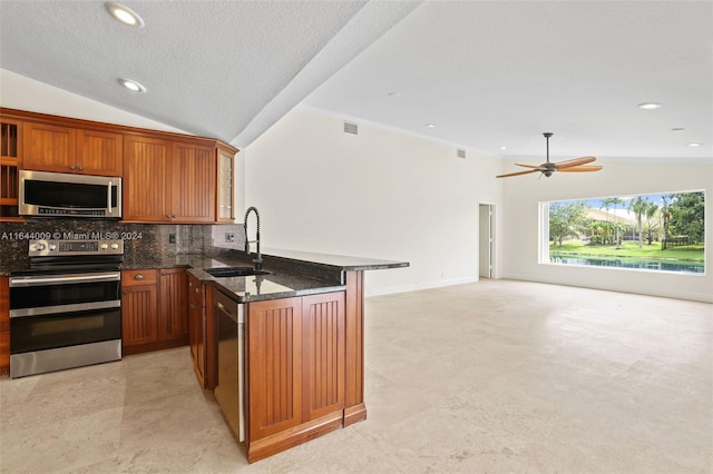 kitchen featuring a textured ceiling, sink, lofted ceiling, appliances with stainless steel finishes, and dark stone countertops