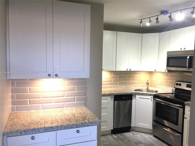 kitchen with light wood-type flooring, light stone counters, stainless steel appliances, white cabinetry, and sink