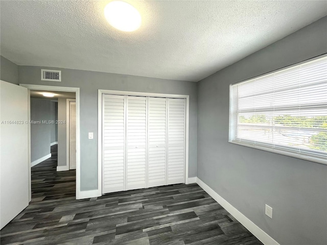 unfurnished bedroom with dark wood-type flooring, a textured ceiling, and a closet