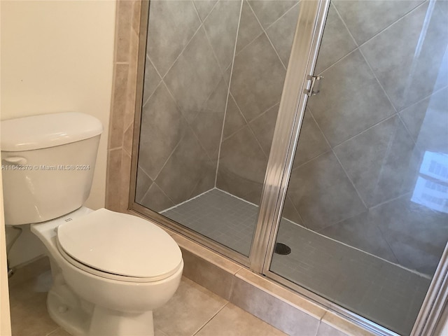 bathroom featuring tile patterned floors, toilet, and a shower with door