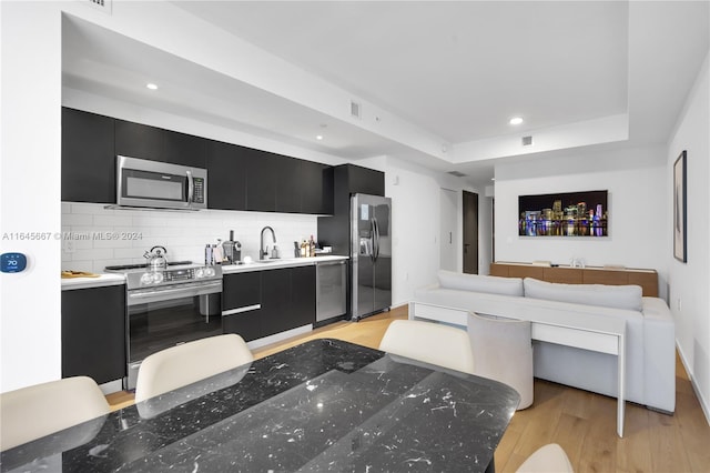 kitchen with appliances with stainless steel finishes, backsplash, sink, and light hardwood / wood-style flooring