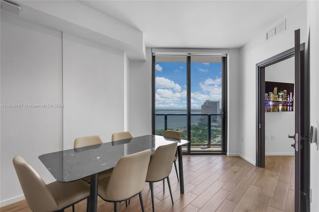 dining area featuring a water view, a wall of windows, and light hardwood / wood-style flooring