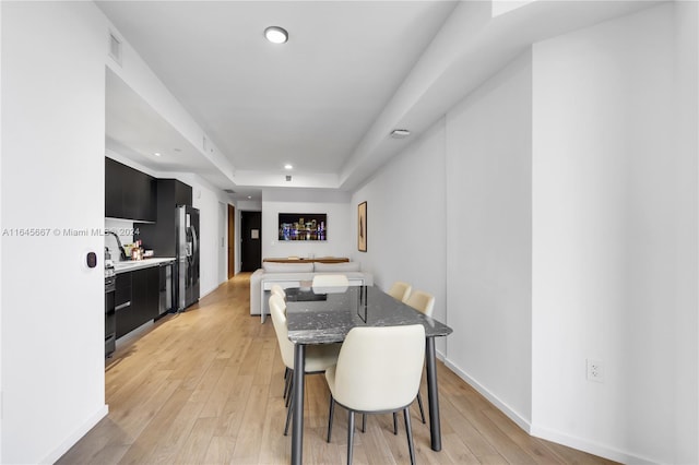 dining area with light wood-type flooring and a tray ceiling