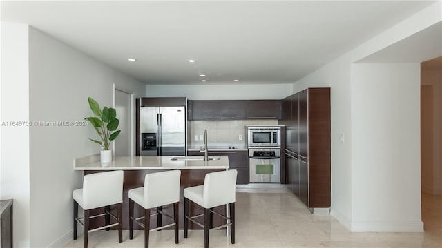 kitchen featuring appliances with stainless steel finishes, backsplash, a kitchen bar, sink, and light tile patterned floors