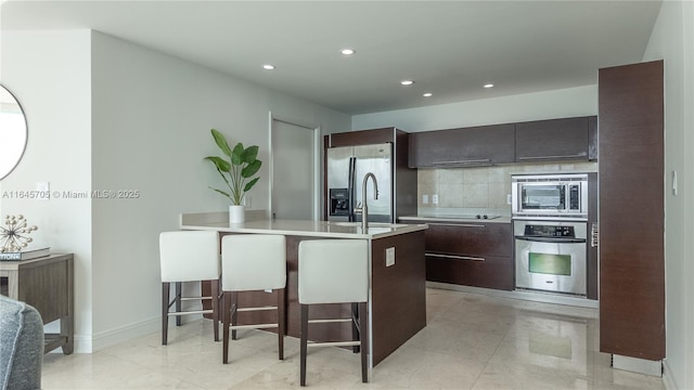 kitchen with tasteful backsplash, an island with sink, sink, a kitchen breakfast bar, and stainless steel appliances