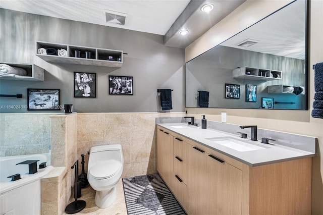 bathroom with tiled bath, dual vanity, tile patterned flooring, tile walls, and toilet