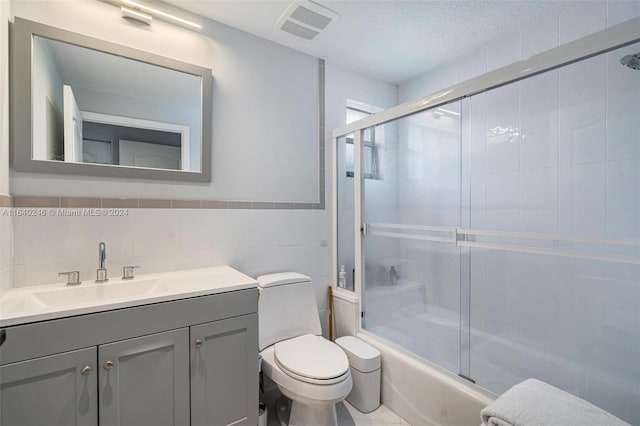 full bathroom with toilet, vanity, tile walls, shower / bath combination with glass door, and a textured ceiling