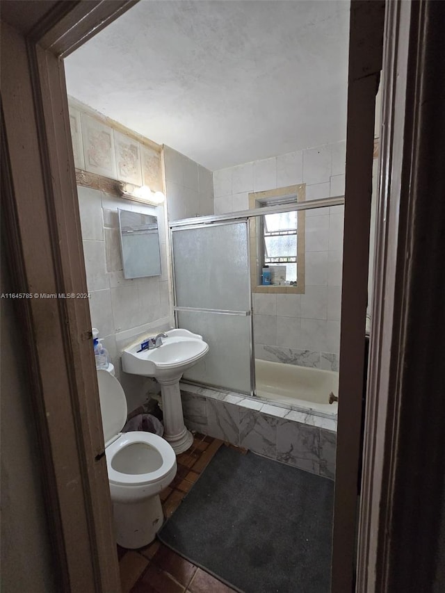 bathroom with tile patterned floors, toilet, tile walls, and combined bath / shower with glass door