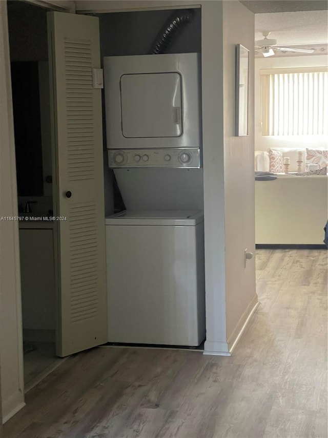 laundry area with light hardwood / wood-style floors, stacked washing maching and dryer, and ceiling fan