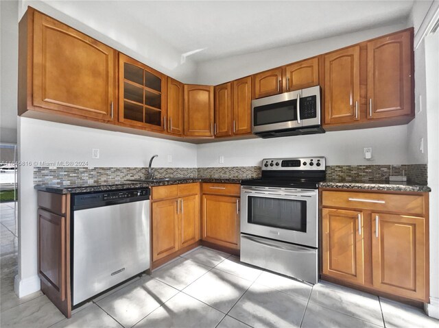 kitchen with sink, dark stone counters, appliances with stainless steel finishes, and light tile patterned floors