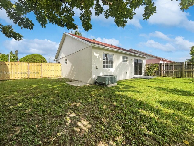 rear view of property featuring central air condition unit and a lawn