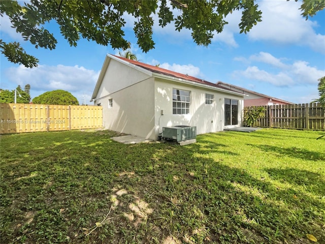 rear view of house featuring central AC, a lawn, a fenced backyard, and stucco siding